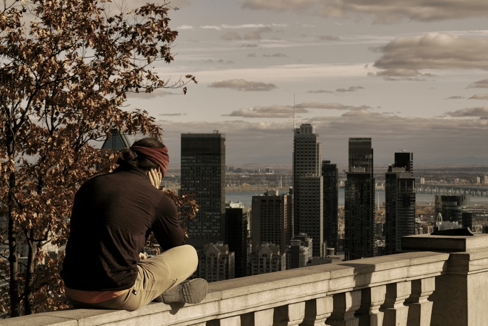 man in black shirt and brown pants sitting on white wooden fence during daytime