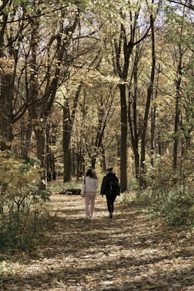 woman in black jacket walking on pathway between trees during daytime