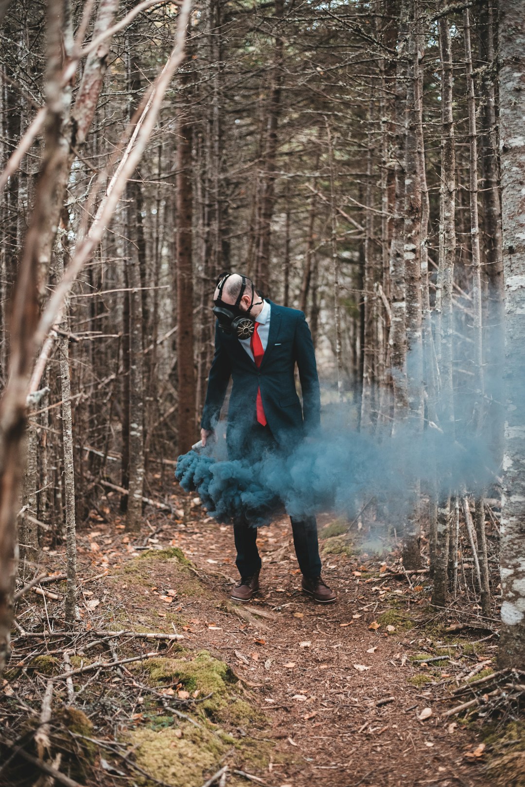 man in black jacket standing on brown dried leaves covered with white smoke