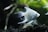 An elegant white fish swims gracefully in an aquarium setting. The fish exhibits long, flowing fins and a streamlined body, set against a backdrop of dark gravel and blurred green aquatic plants.