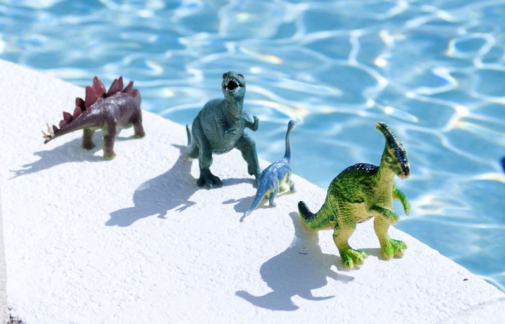 three green and gray animal figurines on white sand during daytime