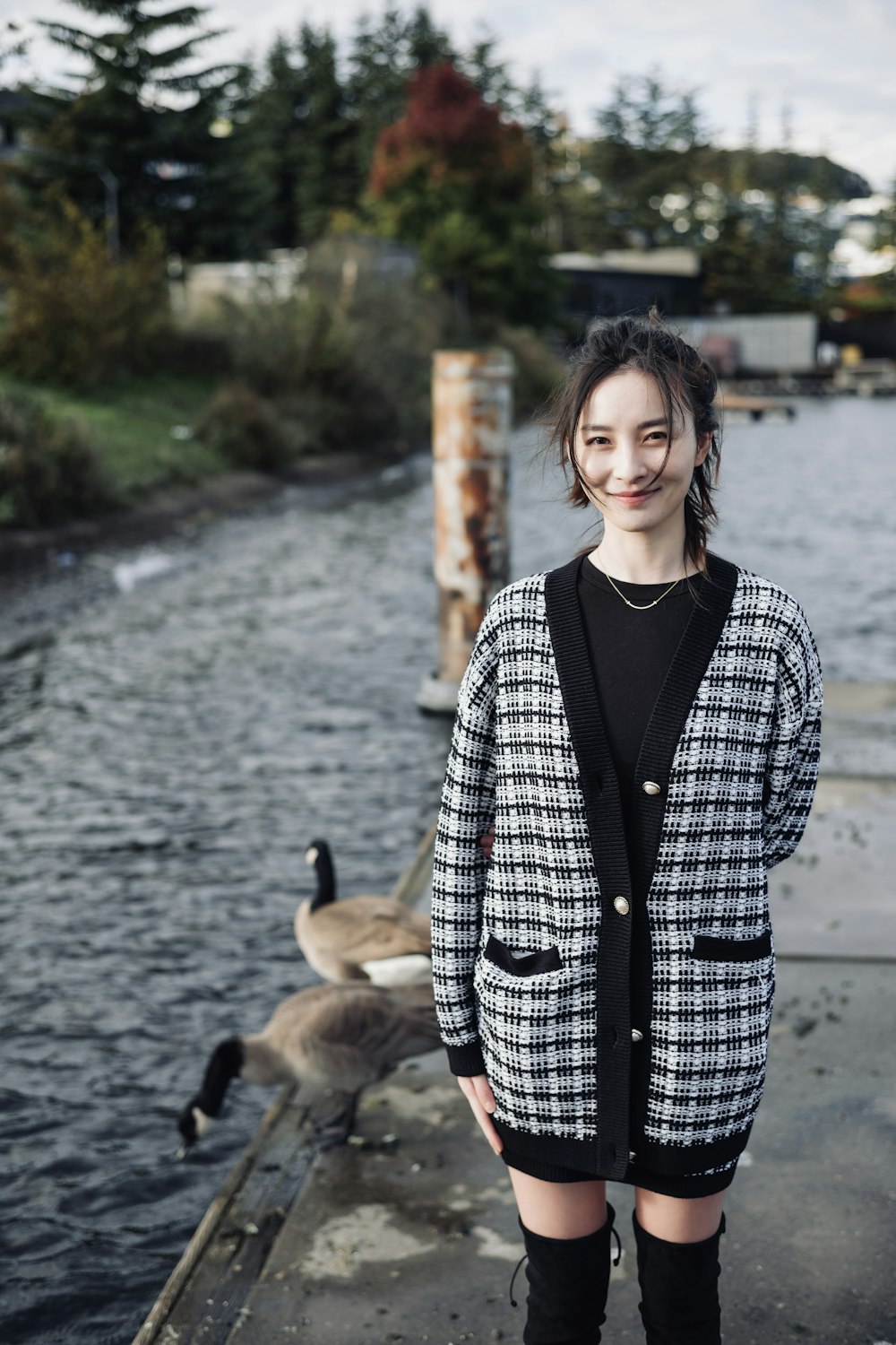 donna in cappotto a scacchi bianco e nero in piedi vicino allo specchio d'acqua durante il giorno