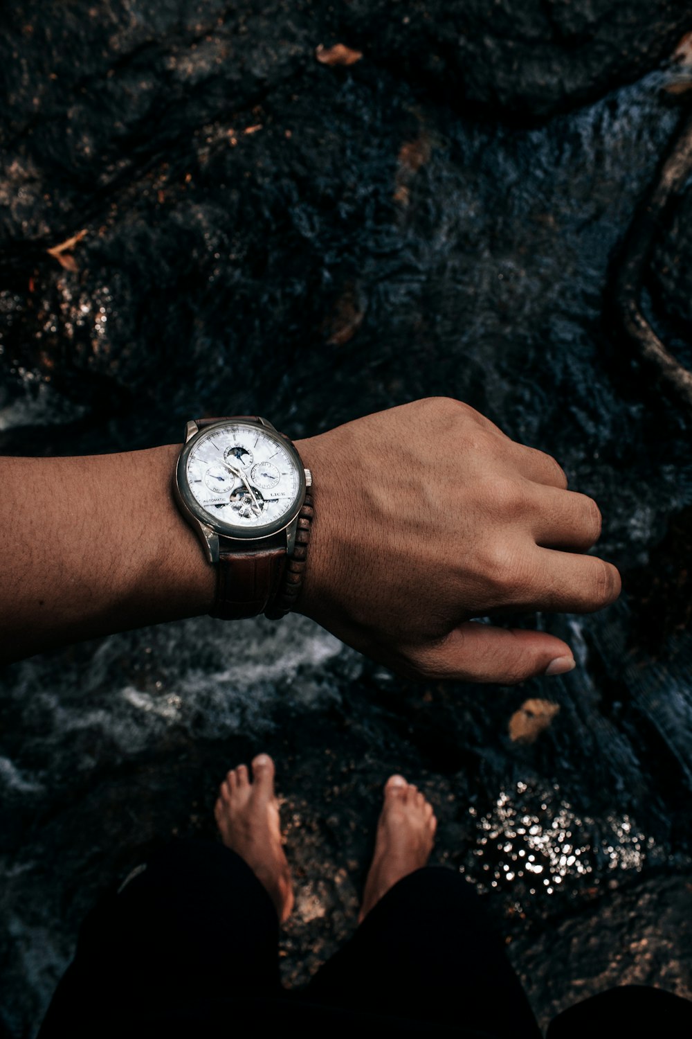 person wearing silver round analog watch with black leather strap