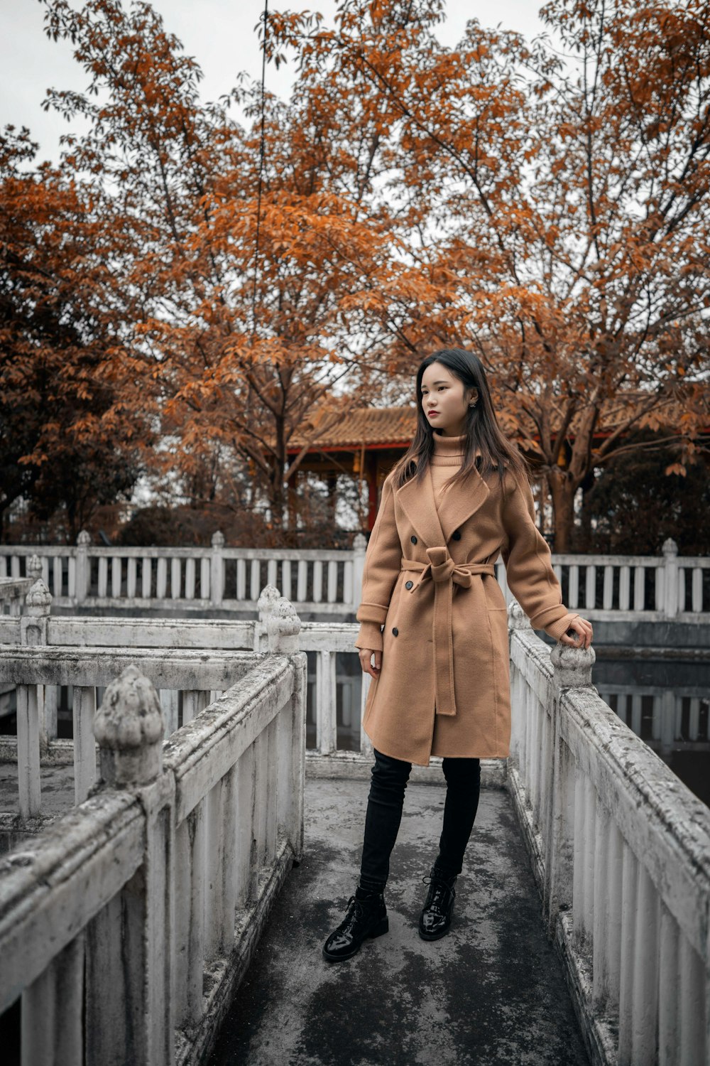 woman in brown coat standing on white bridge during daytime
