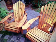 A foldable outdoor chair in warm wood tones, positioned on a sunlit patio with greenery around.
