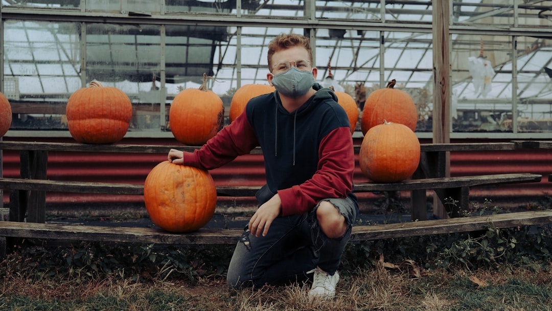 man in blue jacket sitting on brown grass field near pumpkins during daytime