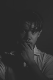 A black and white portrait of a person with a contemplative expression, partially illuminated against a dark background, highlighting facial features and shadows on one side.
