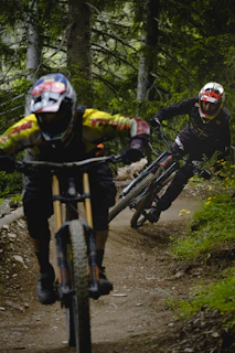 Athletes navigating a rugged trail surrounded by lush green forest during a mountain biking race.