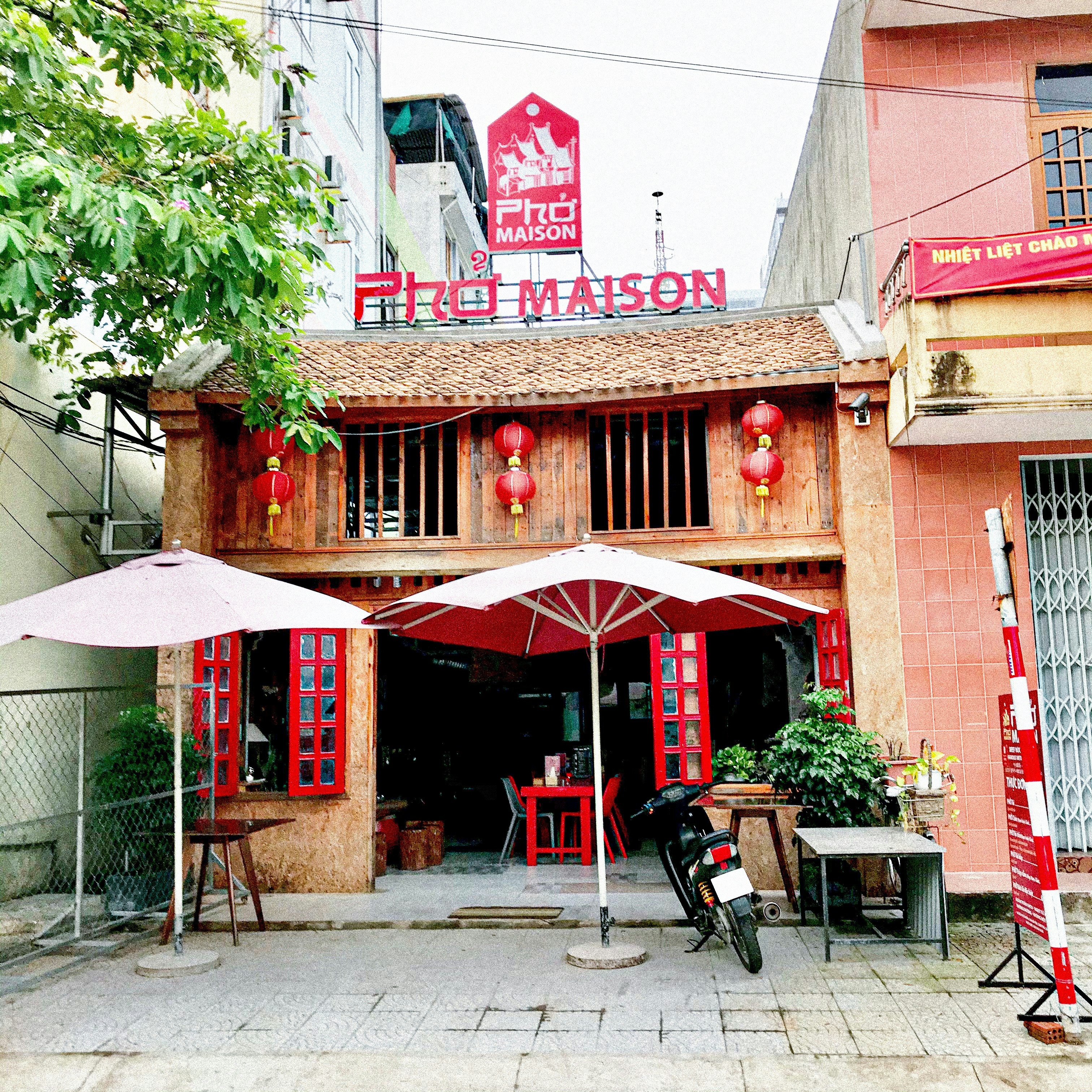 Bright airy Vietnamese restaurant interior with warm wooden furniture, natural light streaming through large windows, and traditional decor