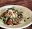 A dish showcasing a creamy burrata cheese atop a bed of roasted cherry tomatoes and fresh greens, drizzled with a rich balsamic glaze and green pesto. The meal is presented on a simple white plate, highlighting the colorful ingredients.