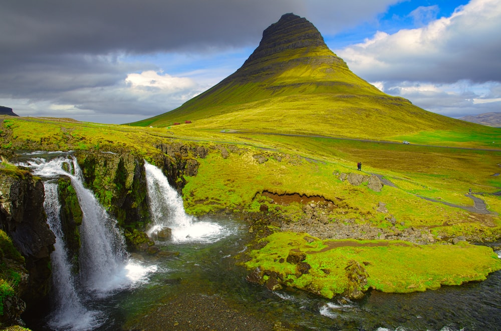 waterfalls in green grass field under white clouds and blue sky during daytime