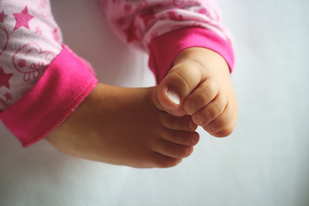 A close-up view of small, delicate baby feet wearing pink pajamas adorned with star patterns on a soft, neutral background.