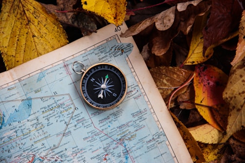 A compass resting on a weathered wooden table beside a folded map.