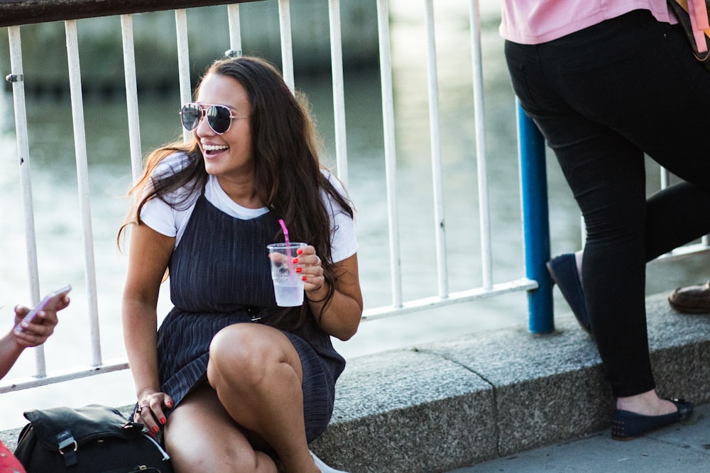 woman in black tank top and blue denim shorts wearing black sunglasses sitting on concrete bench