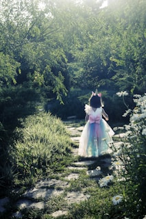 A joyful child wearing a mint green princess gown, playing in a sunlit garden with flowers.