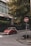 A red compact car is parked on a city street near a tall building with the sign 'UniCredit Bulbank'. The street is lined with stone bollards and has a stop sign with a graphic. Green trees with yellowing leaves are visible in the background, adding a touch of nature to the urban setting.