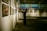 An art gallery with several framed paintings displayed on the walls. A person stands in front of the artwork, seemingly taking pictures or observing closely. The lighting is soft and focused on the paintings, creating a serene and contemplative atmosphere.