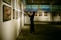 An art gallery with several framed paintings displayed on the walls. A person stands in front of the artwork, seemingly taking pictures or observing closely. The lighting is soft and focused on the paintings, creating a serene and contemplative atmosphere.