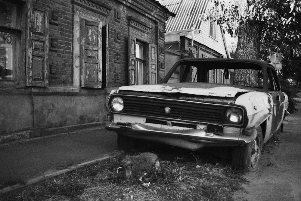grayscale photo of vintage car parked beside house