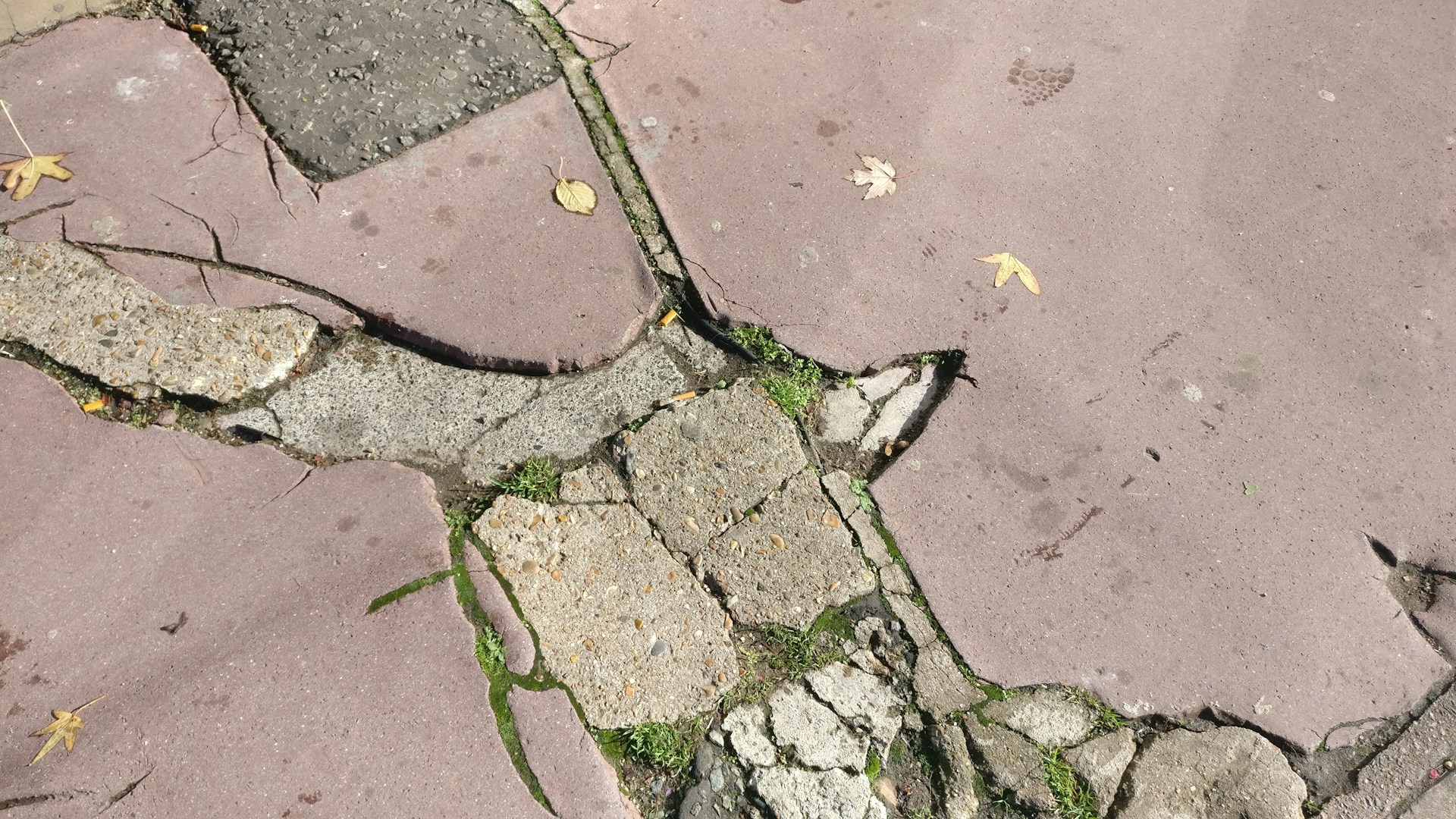 A close-up shot of a crumbling public sidewalk with visible cracks and debris, highlighting poor city maintenance.