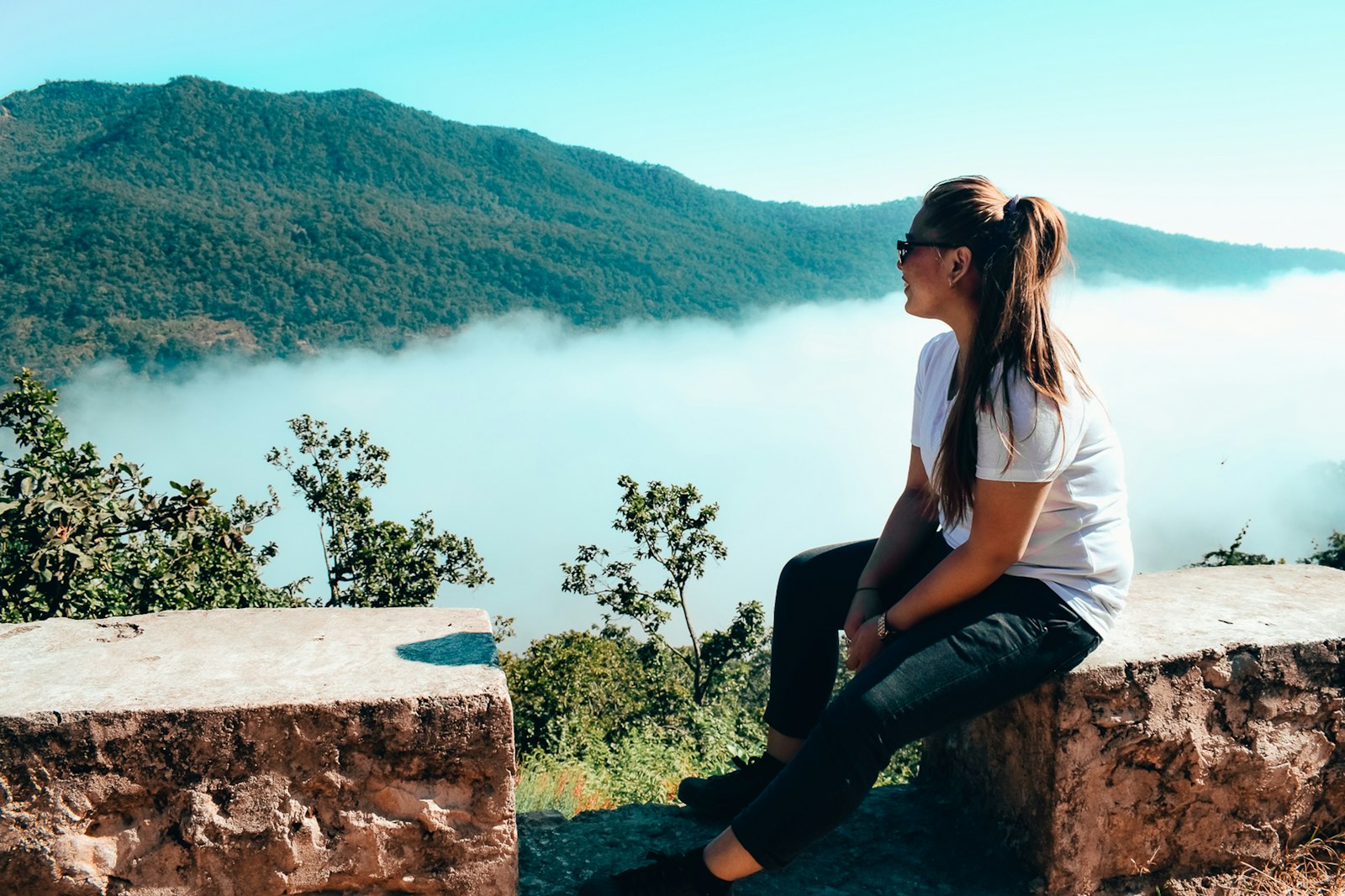 Smiling woman sitting on a ledge, enjoying a misty valley view