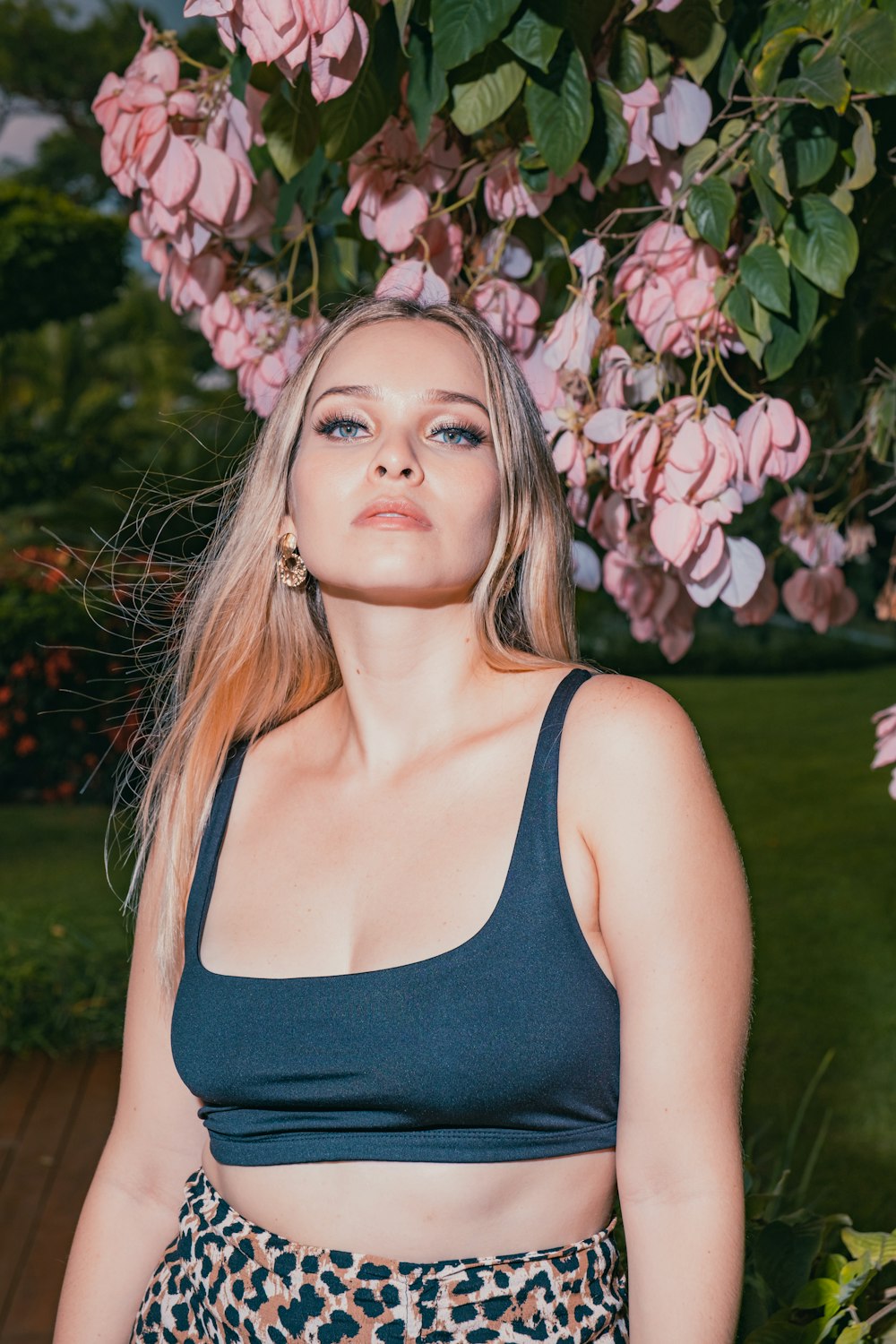 woman in black tank top standing beside pink flowers