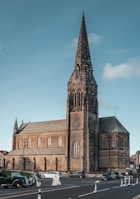 A weathered church steeple peeking behind a row of shiny muscle cars.