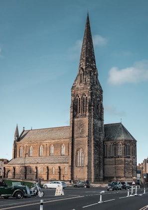 A weathered church steeple peeking behind a row of shiny muscle cars.