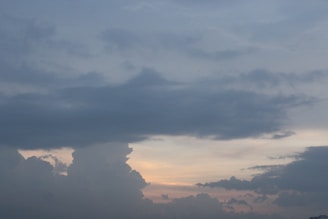 Dark, thick clouds dominate the sky with a hint of sunlight peeking through near the horizon, suggesting a potential sunset or sunrise. The overall atmosphere appears calm yet somewhat ominous due to the heavy cloud cover.