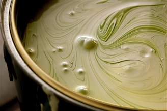 A close-up view of a paint can filled with light green paint. The surface features swirling patterns and bubbles, creating a textured appearance.