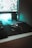 A computer setup featuring a mechanical gaming mouse with illuminated accents on a black mouse pad. The mouse is positioned next to a keyboard, and a monitor displays a blurry, colorful background. Ambient teal lighting creates a futuristic and gaming-themed atmosphere.