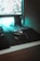 A computer setup featuring a mechanical gaming mouse with illuminated accents on a black mouse pad. The mouse is positioned next to a keyboard, and a monitor displays a blurry, colorful background. Ambient teal lighting creates a futuristic and gaming-themed atmosphere.