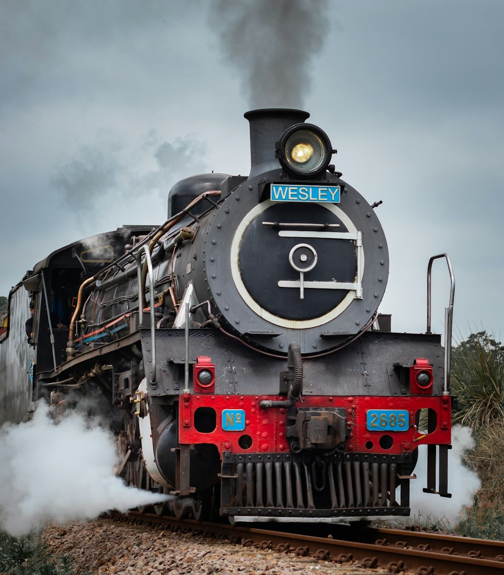 昼間の曇り空の下、線路を走る黒と赤の列車