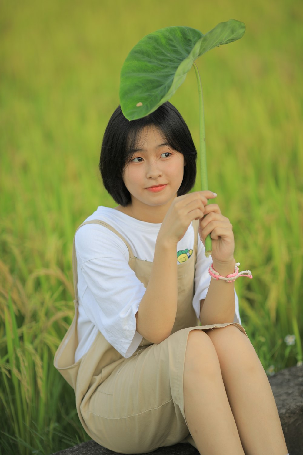 woman in white t-shirt and white shorts sitting on grass field holding green umbrella during