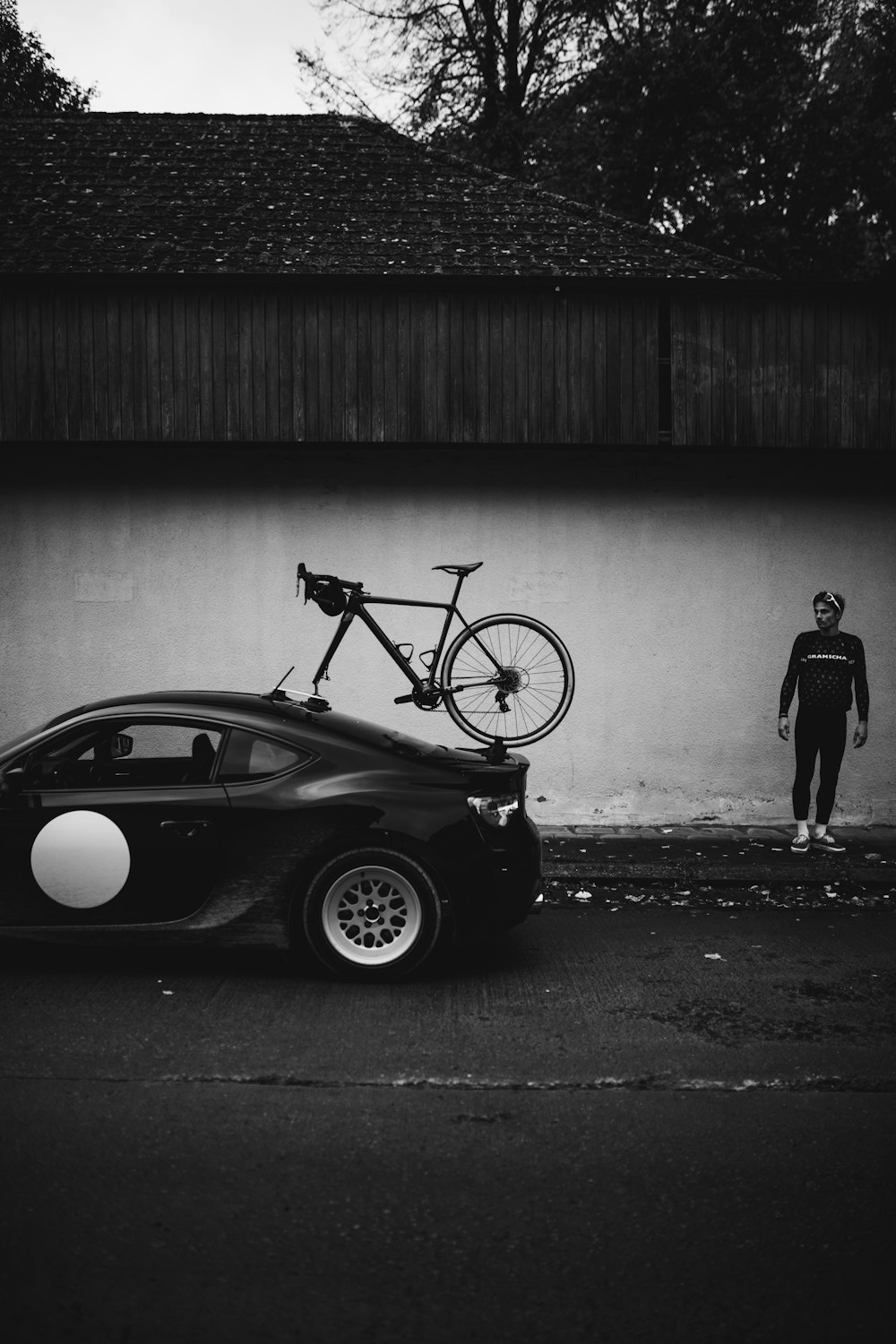 grayscale photo of man standing beside car