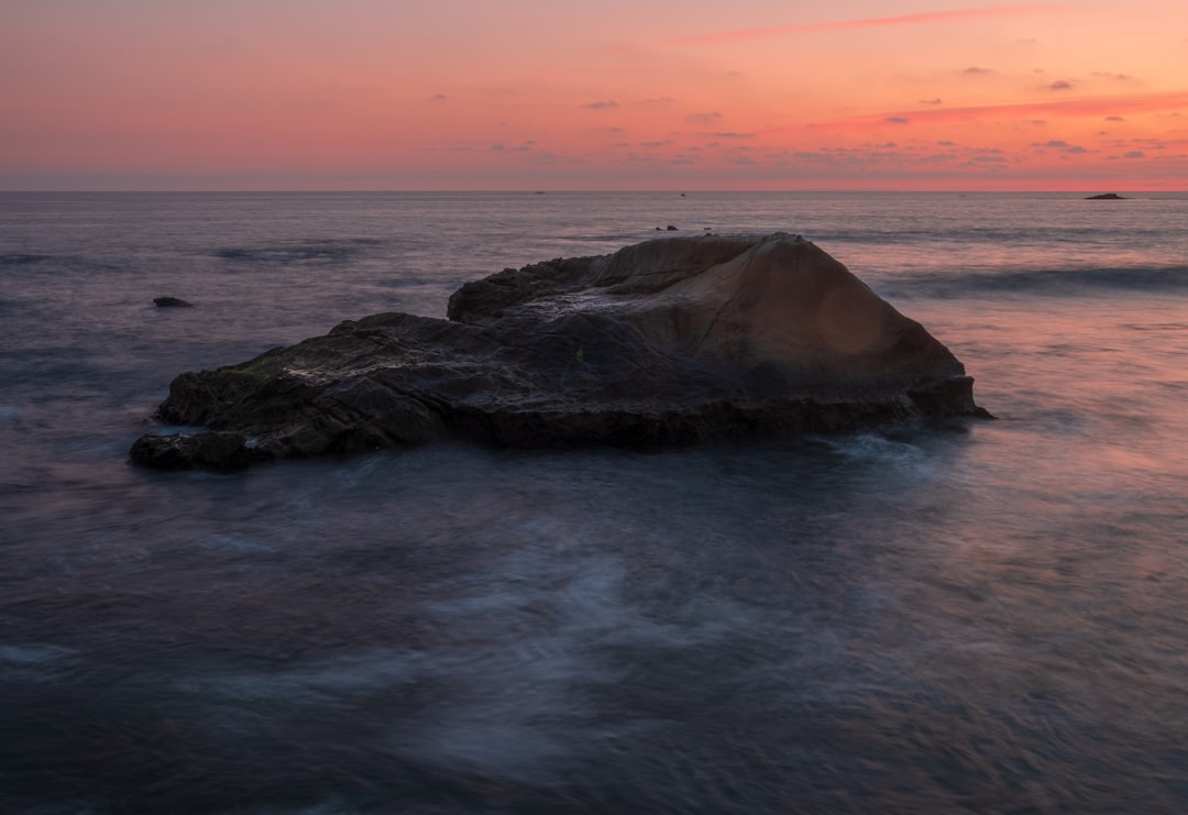 black rock formation on sea during sunset