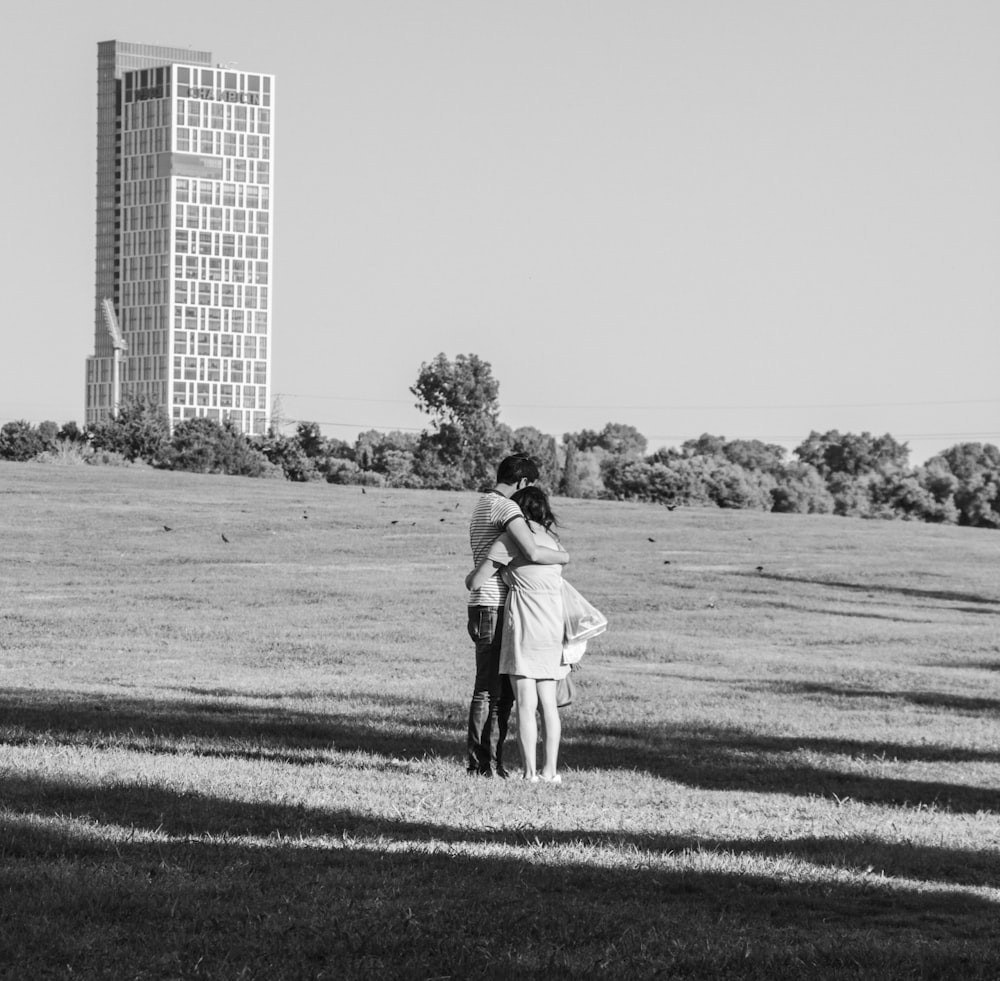 grayscale photo of man and woman walking on grass field