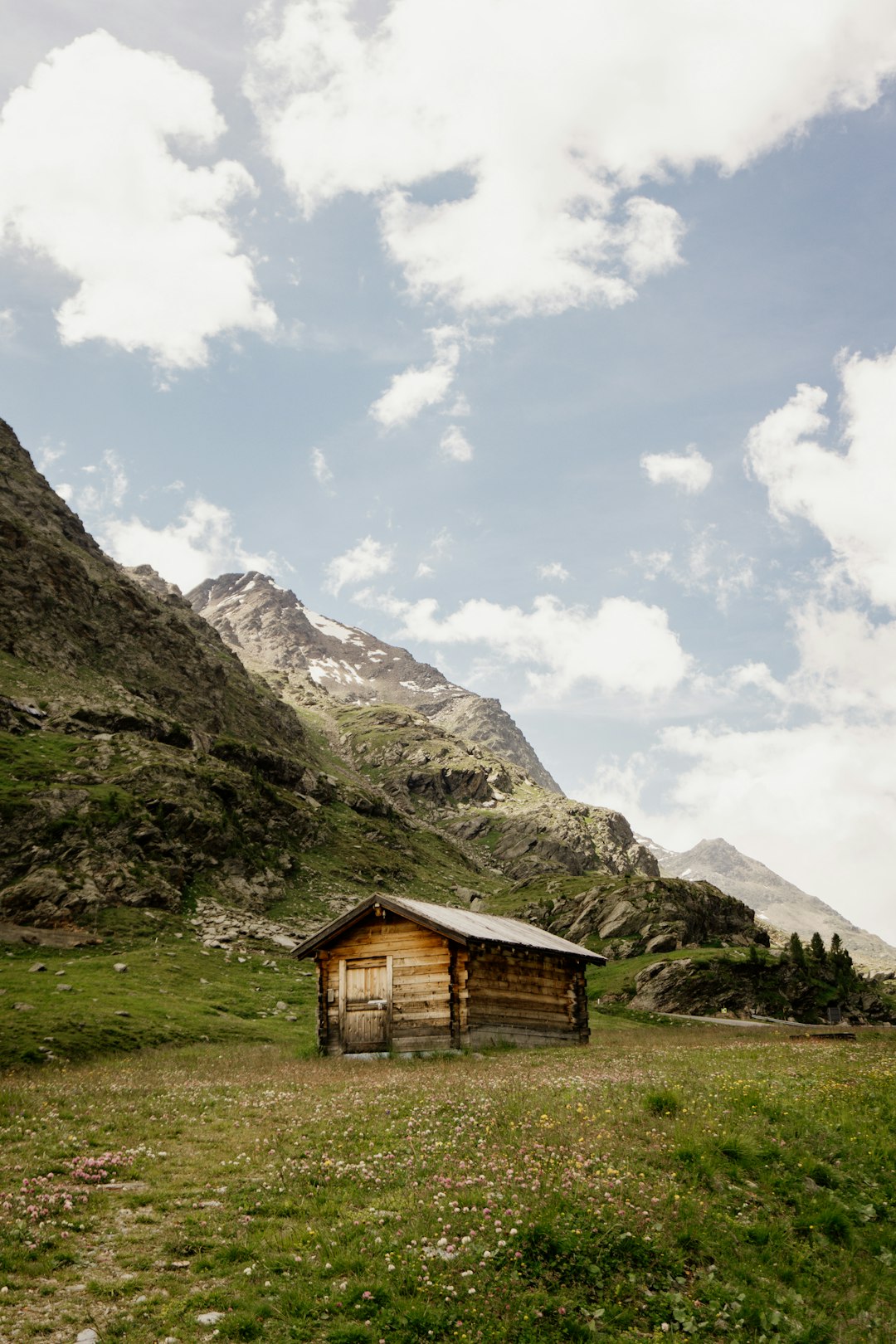 brown wooden house on green grass field near gray rocky mountain under white cloudy sky during