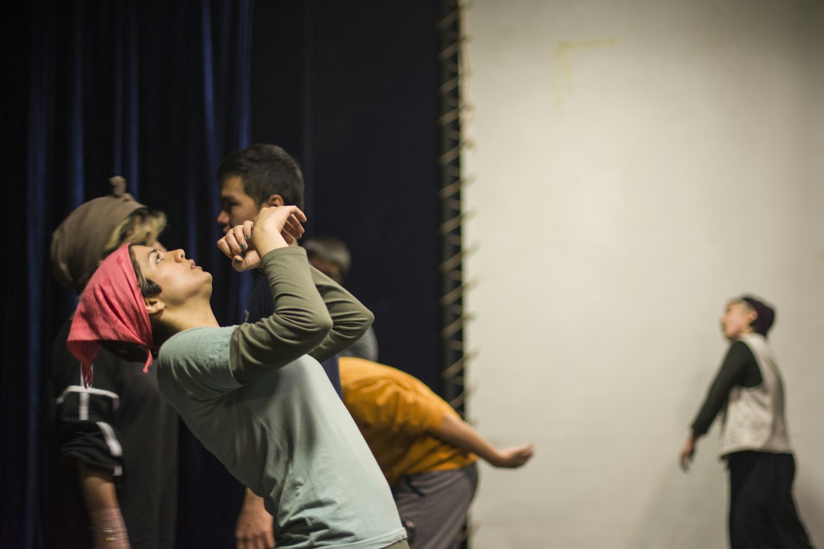 Actors in rehearsal clothes stretching and reaching in a bare studio