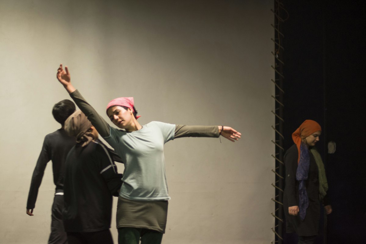 A performer in a headscarf reaching up joyfully while the cast moves around her