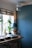 A cozy interior corner featuring a blue wall and a window with bamboo blinds. A wooden table holds a record player, a pair of headphones on a stand, two potted plants, and a decorative flamingo statue. A disco ball hangs from the ceiling, casting subtle reflections.