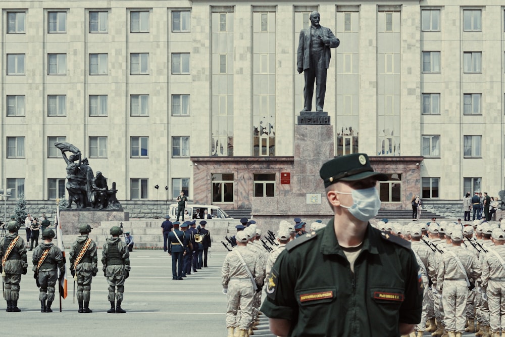 man in green and brown camouflage uniform standing near people in front of building during daytime