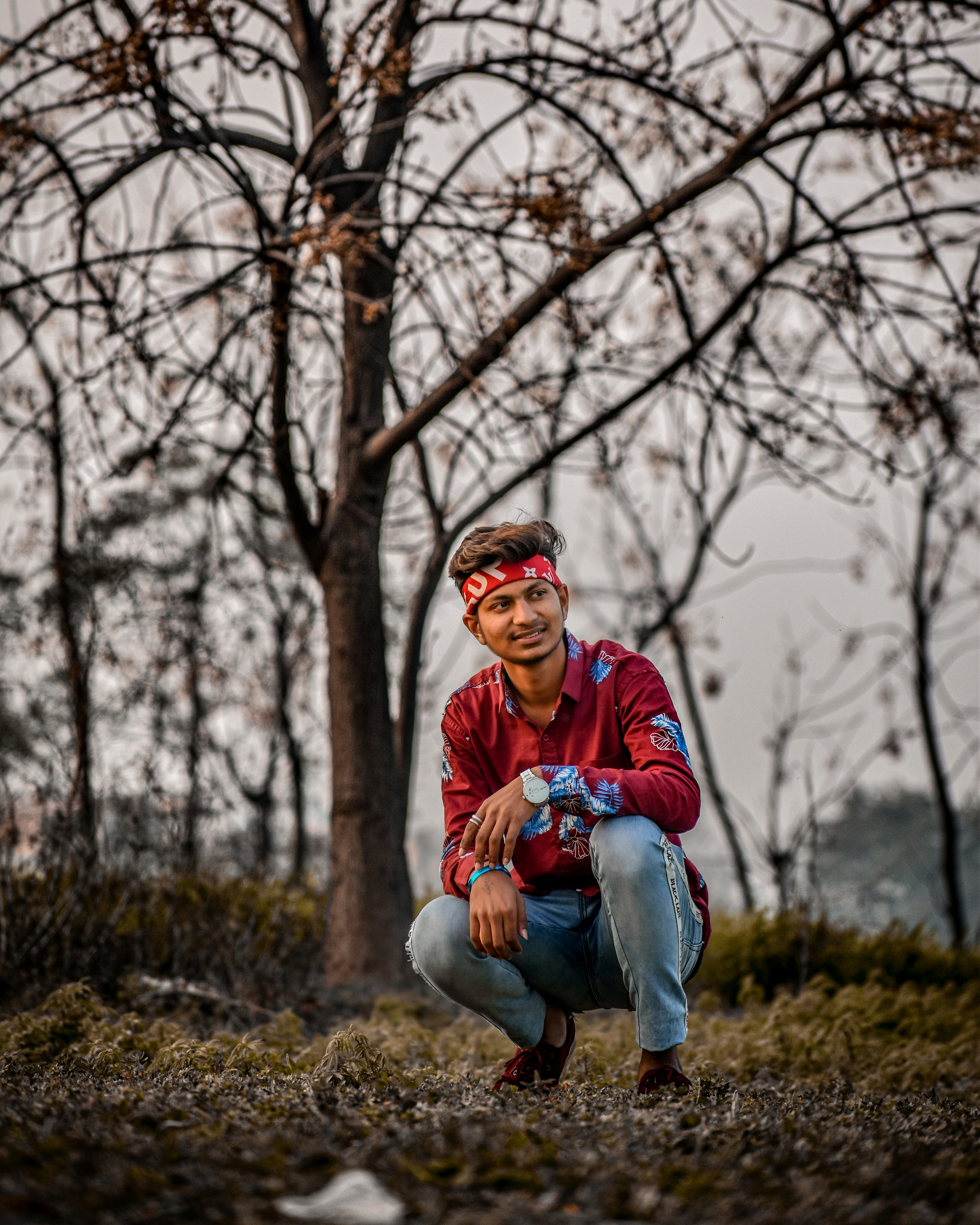 Pria berjaket merah duduk di lapangan rumput coklat di siang hari