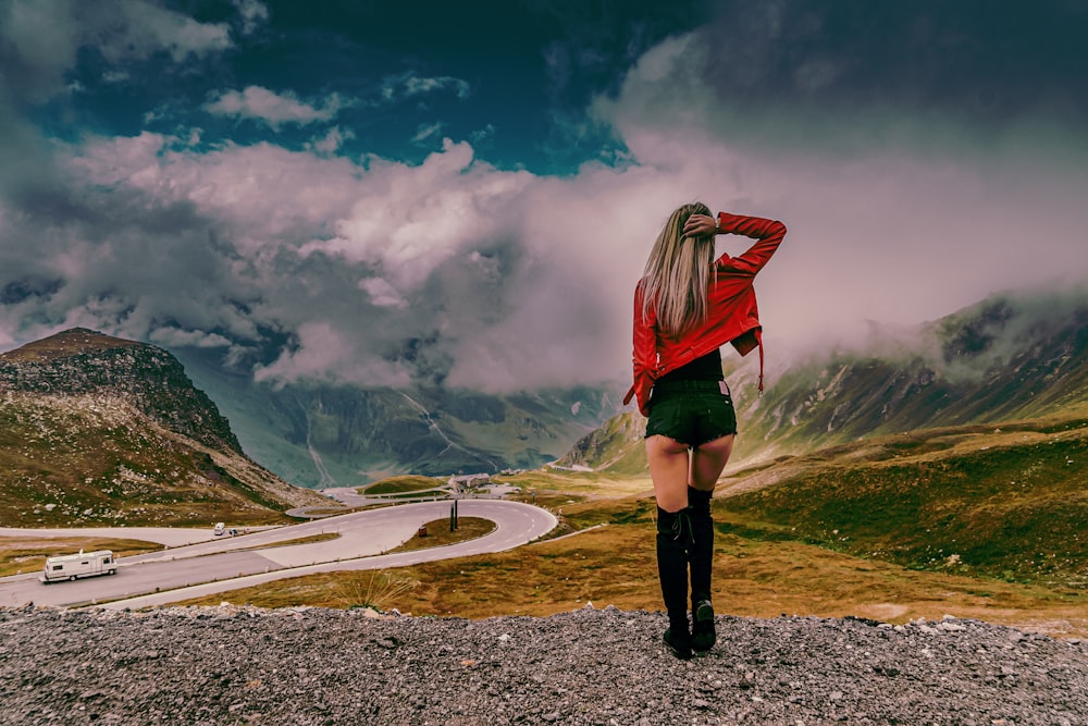 woman in red jacket and black pants standing on gray concrete road during daytime