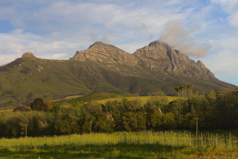 green grass field near mountain under white clouds during daytime