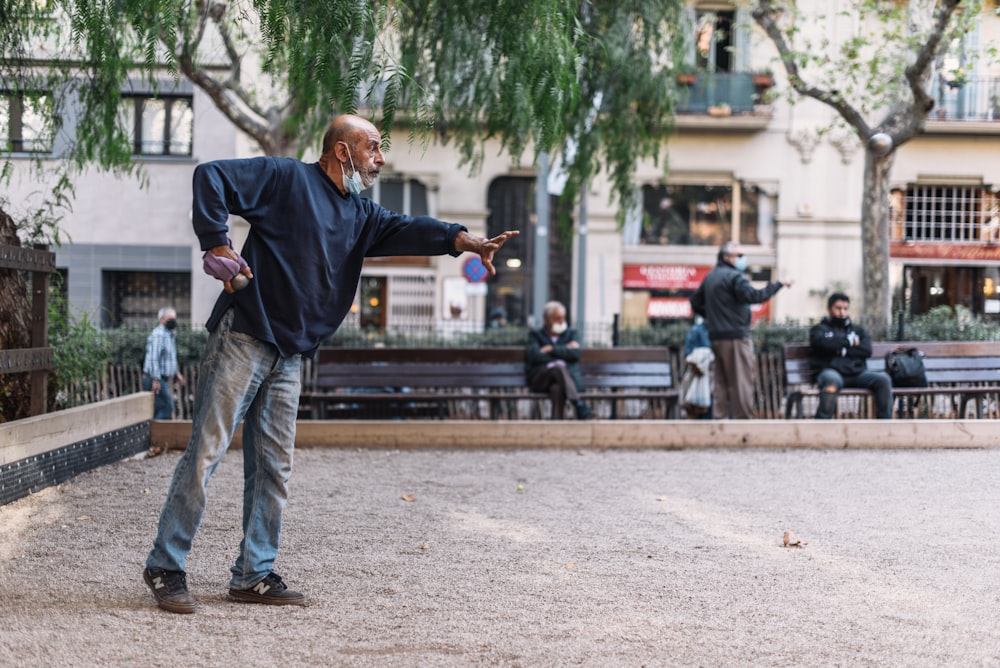 homme en veste noire et jean bleu debout sur le sol en béton gris pendant la journée