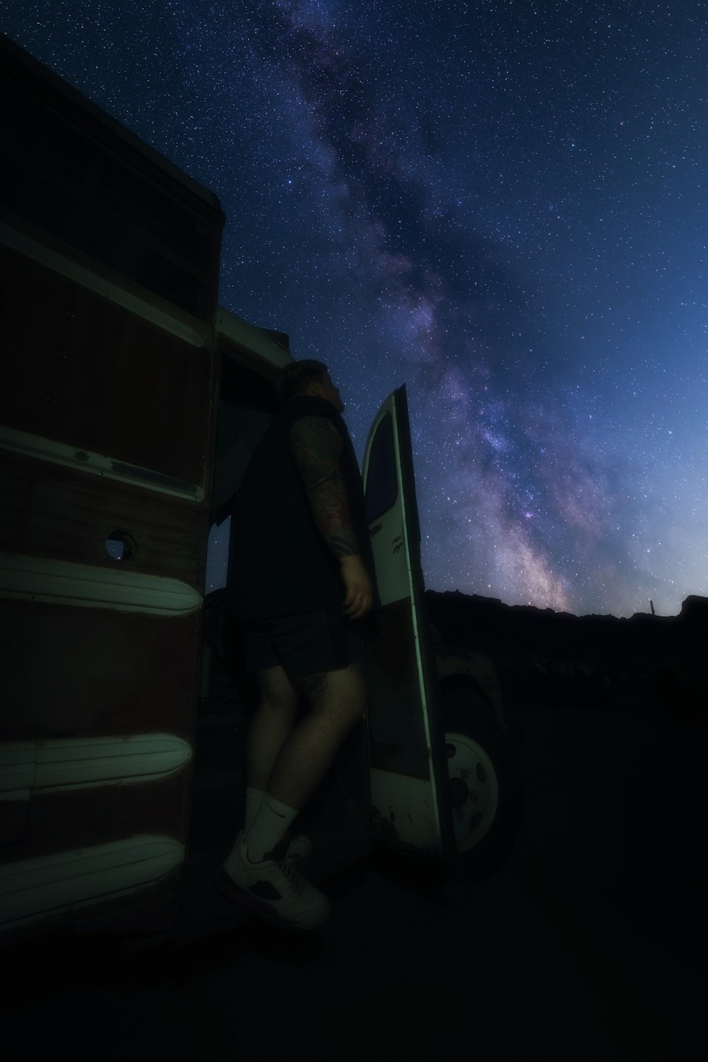 man in black shorts sitting on white and black car under starry night