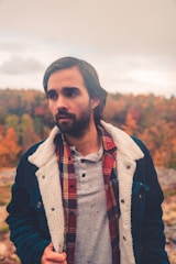 A man wearing a layered sweater outfit while enjoying a coffee outdoors on a chilly day.