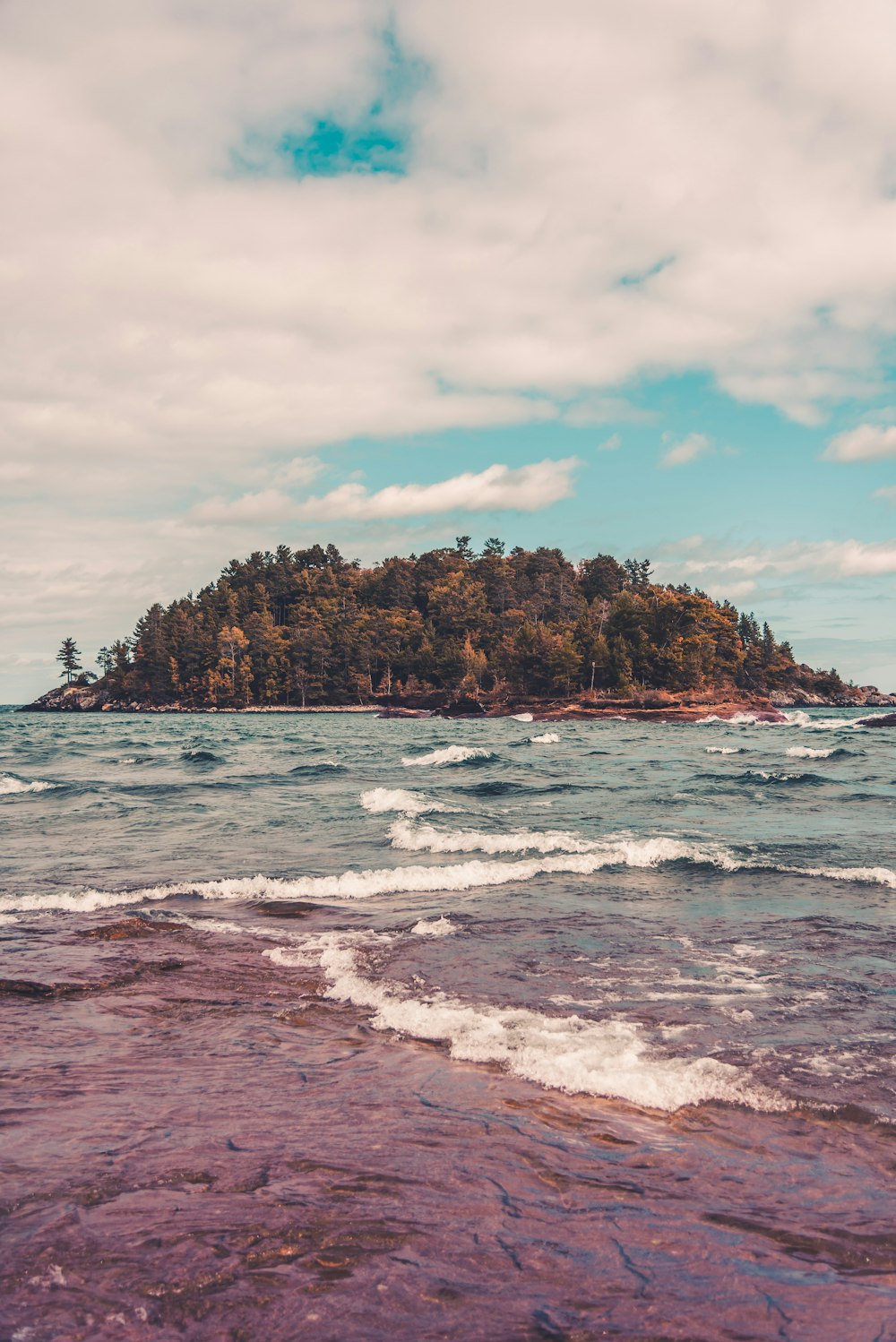 brown and green island on sea under white clouds and blue sky during daytime