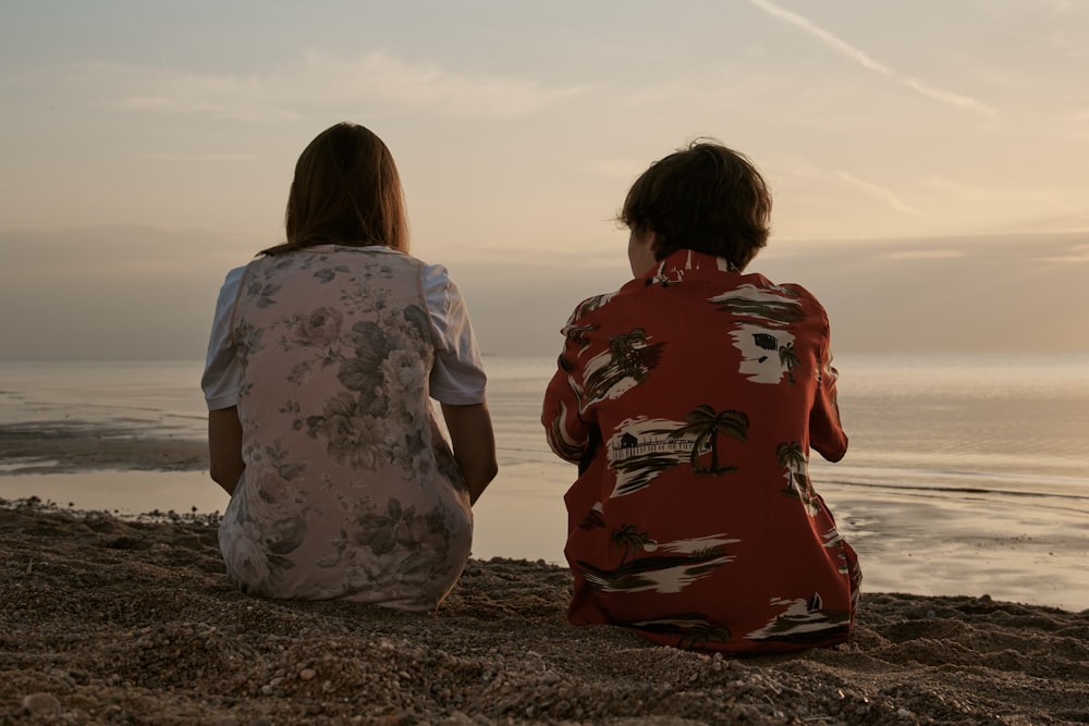 2 women sitting on brown sand during daytime